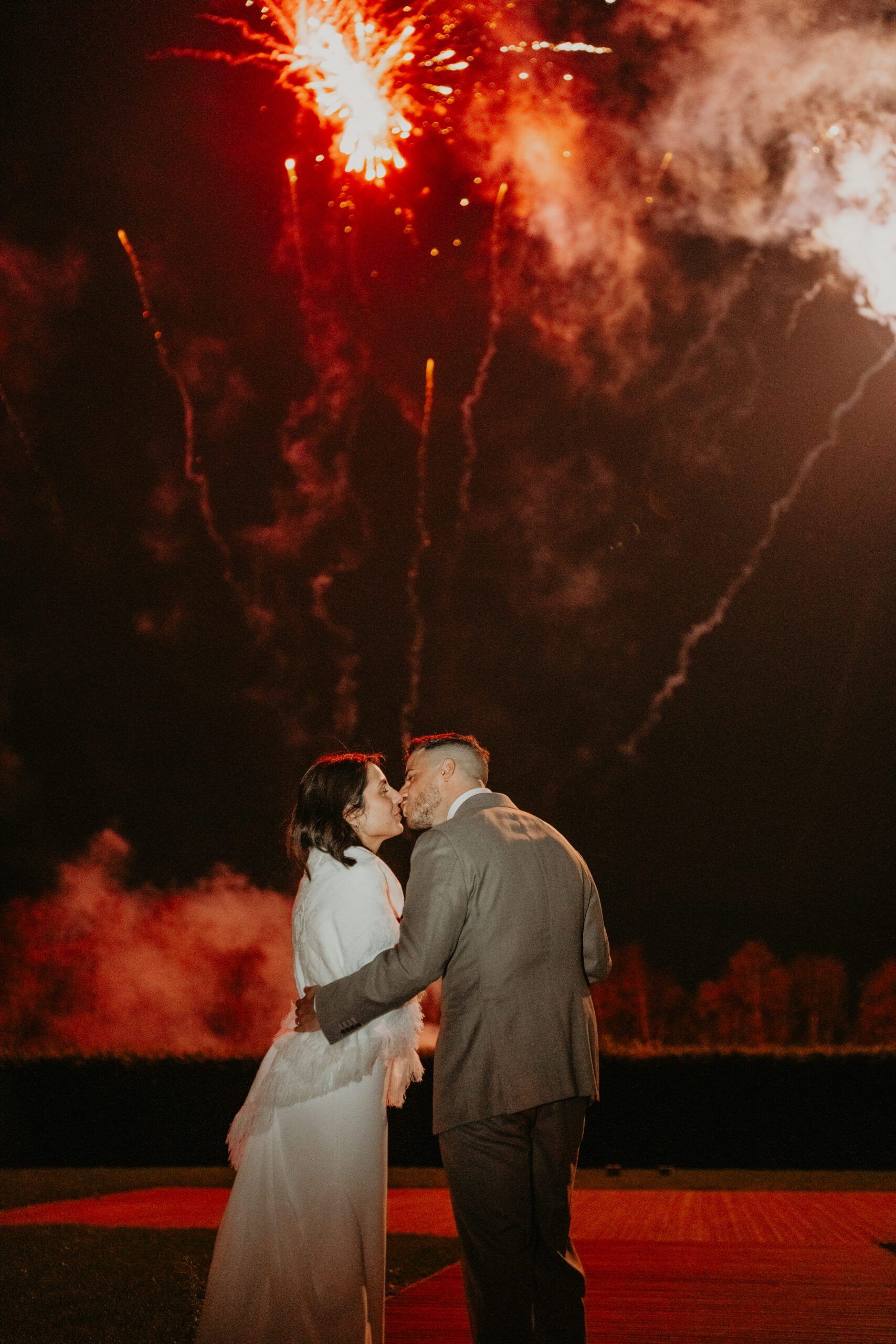 Les mariés s’embrassent devant un feu d’artifice, à la nuit tombée.