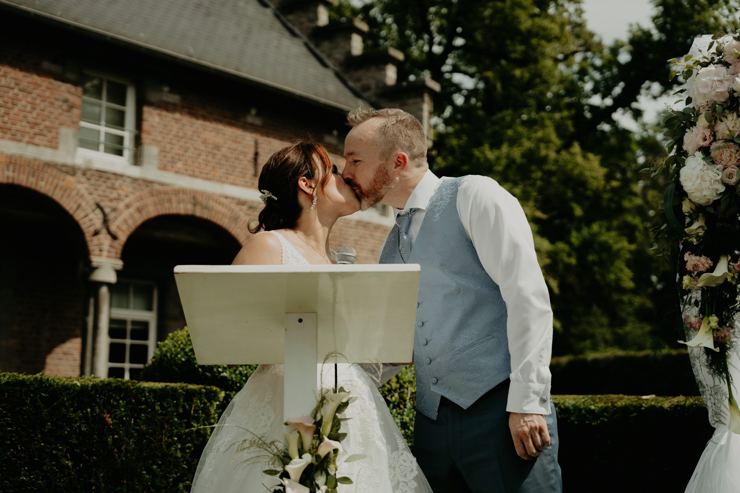 Laura et Benoît s’embrassent derrière le pupitre de la cérémonie, devant les arcades de brique du château.