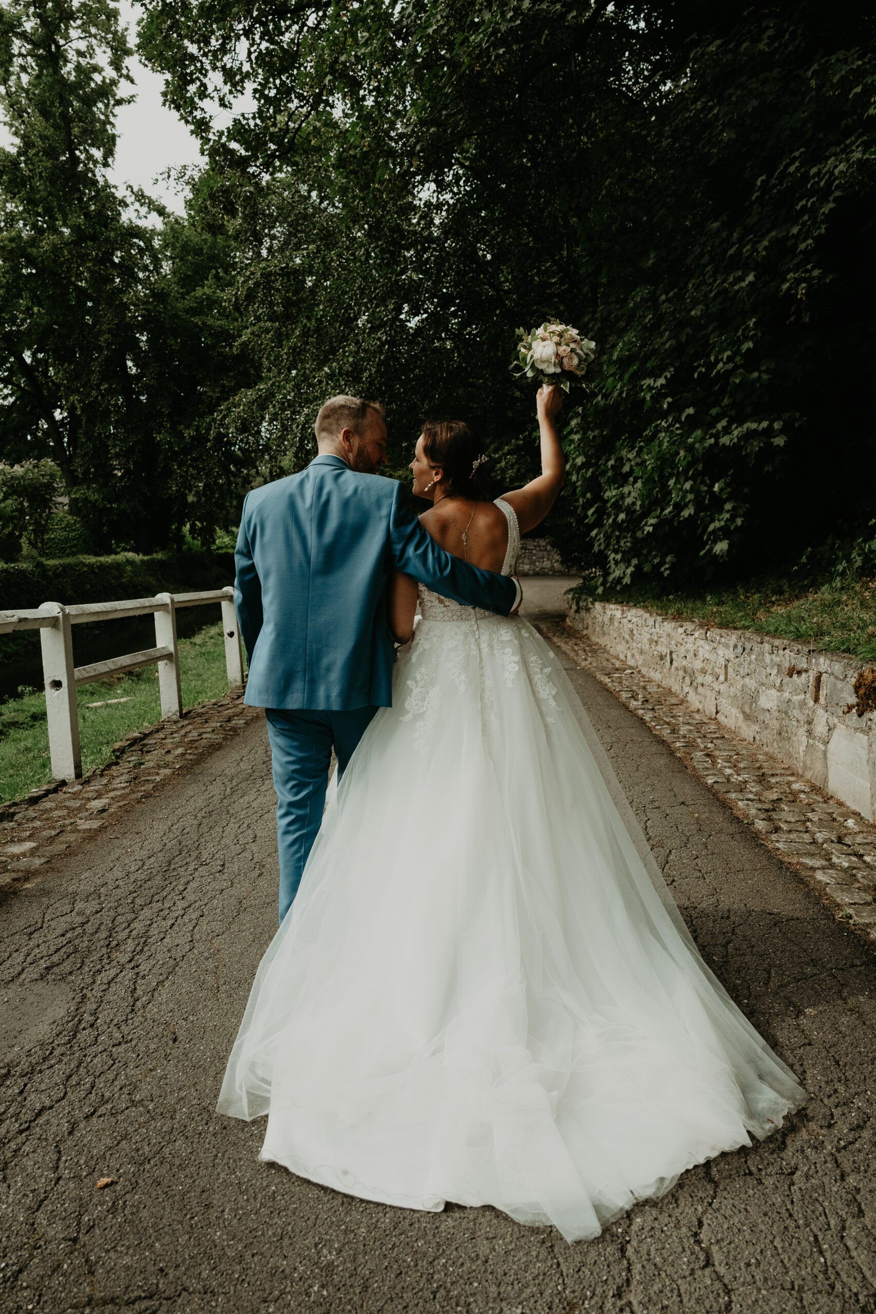 Les mariés s’éloignent sur un chemin, la mariée lève son bouquet.