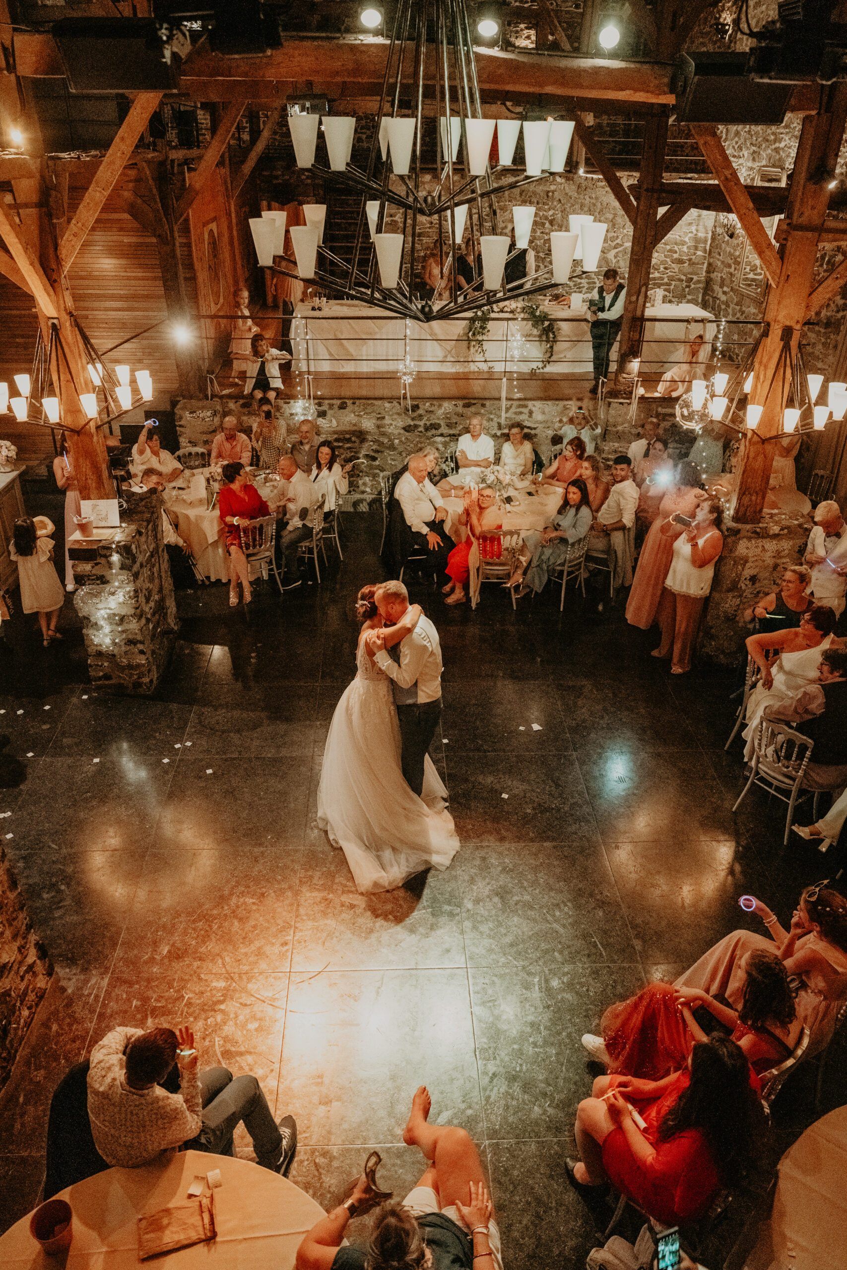 Vue d’en haut, la première danse des mariés au milieu des invités, dans une salle aux poutres de bois.