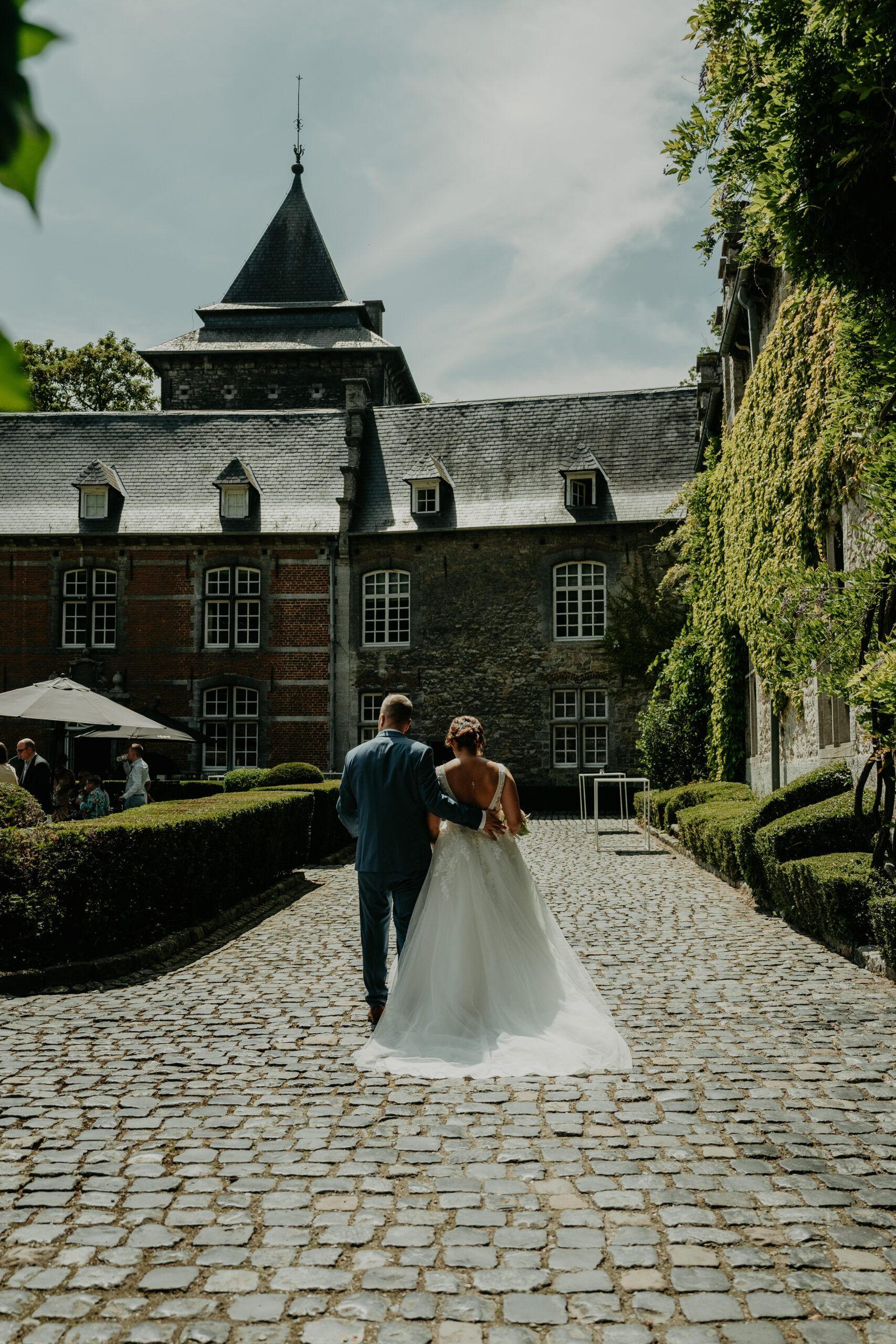 Les mariés marchent, de dos, sur les pavés qui mènent au château.